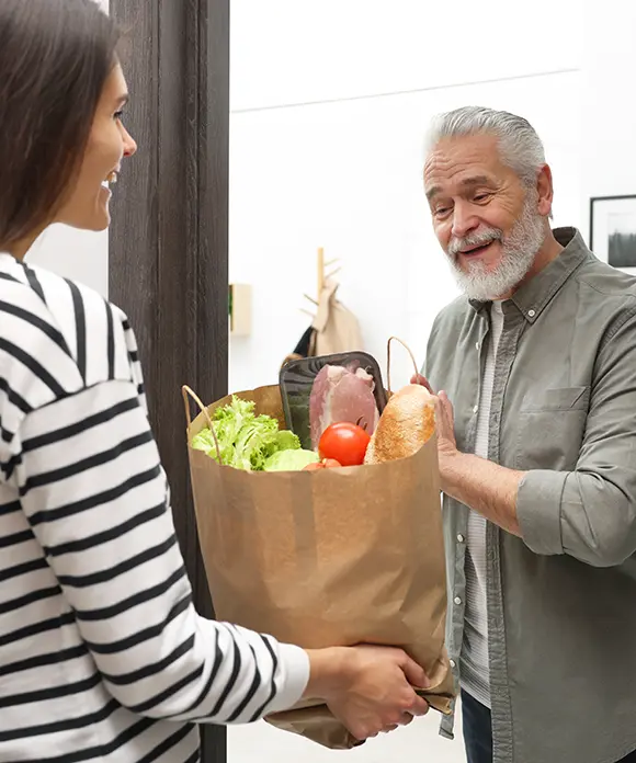 Eine Junge Frau übergiebt einem Senior die Einkäufe